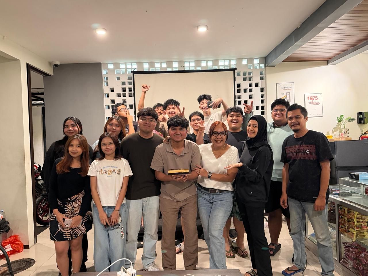 Penghuni dan owner berkumpul merayakan ulang tahun di communal area, satu orang memegang kue di depan dinding roster putih